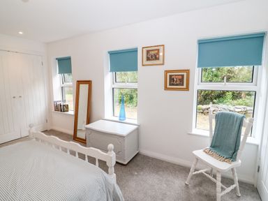 A bedroom with a bed a white chest a white chair with a blanket a standing mirror and three windows with blue blinds at Kealduff Lower in Glenbeigh County Kerry