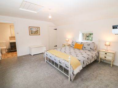 A bedroom with a bed a yellow pillow two bedside tables with lamps a chest and a bathroom visible at Kealduff Lower in Glenbeigh County Kerry