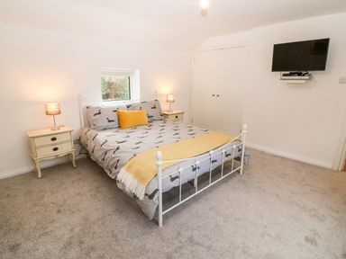 A bedroom with a bed with dog print bedding two bedside tables with lamps a wall mounted TV and carpeted floor at Kealduff Lower Glenbeigh County Kerry