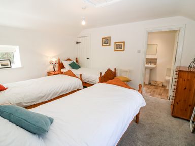 A bedroom with three single beds a bedside table with a lamp a small window a wooden dresser and an open door to a bathroom at Kealduff Lower in Glenbeigh County Kerry