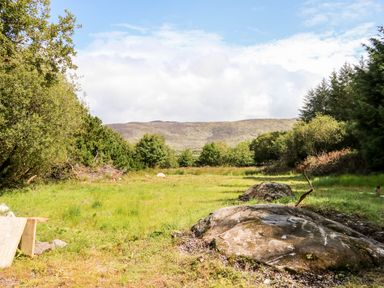 A grassy open area with rocks and bushes surrounded by trees and hills in the background at Kealduff Lower Glenbeigh County Kerry