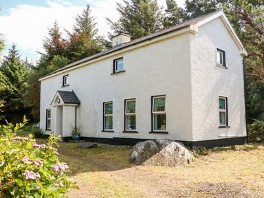 A white house with black window frames surrounded by trees and plants at Kealduff Lower in Glenbeigh County Kerry