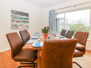 A dining room with a wooden table set for eight and large window with blue curtains at Casalmare in Exmouth
