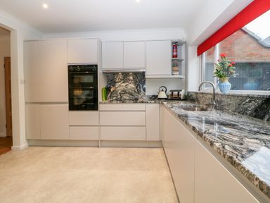 A kitchen with grey cabinets a granite countertop built in oven and a window with a red blind at Casalmare in Exmouth