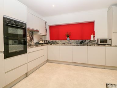 A kitchen with white cabinets black double oven granite countertops a microwave and a window with a red blind at Casalmare in Exmouth