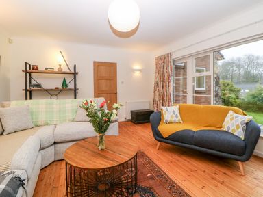 A living room with two sofas a wooden coffee table with flowers a wooden floor and a window showing a garden at Casalmare in Exmouth