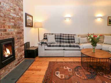 A living room with a brick fireplace a gray sofa with cushions a wooden coffee table with flowers and a patterned rug at Casalmare in Exmouth