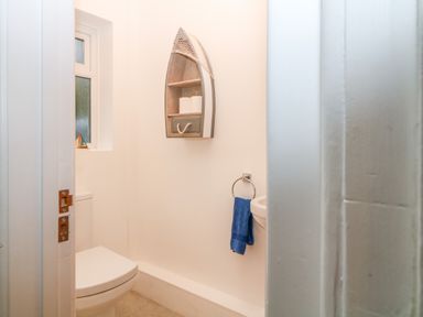 A small bathroom with a toilet a window a boat shaped shelf with toilet paper and a blue towel on a ring at Casalmare in Exmouth