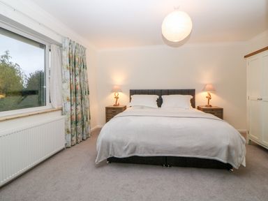A bedroom with a double bed between two bedside tables with lamps a large window with floral curtains and a white wardrobe at Casalmare in Exmouth