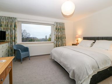 A bedroom with a bed side lamp a large window a blue chair and a wooden table at Casalmare in Exmouth