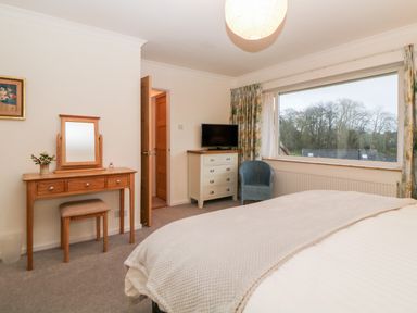 A bedroom with a dressing table and stool a chest of drawers a chair and a window showing trees outside at Casalmare in Exmouth