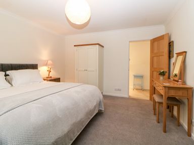 A bedroom with a bed a nightstand with a lamp a wardrobe and a wooden dressing table with a mirror and stool at Casalmare in Exmouth