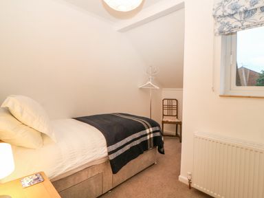 A bedroom with a single bed covered by a dark blanket a wooden chair a coat stand and a window at Casalmare in Exmouth