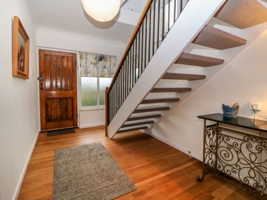 An entryway with a wooden front door a window with a patterned shade a staircase with carpeted steps a rug on a wooden floor and a black metal table at Casalmare in Exmouth