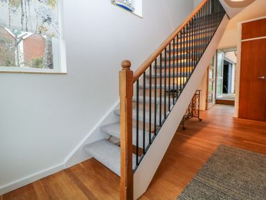 A hallway with wooden floor a carpet and staircase with wooden handrail and black balusters at Casalmare in Exmouth