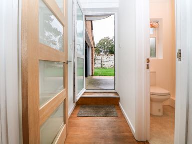 A hallway with wooden floor and glass panel door leading to an outside garden and a small bathroom with a toilet at Casalmare in Exmouth