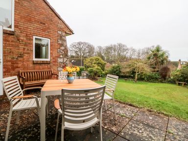 An outdoor patio with a table and chairs next to a brick house overlooking a garden at Casalmare in Exmouth