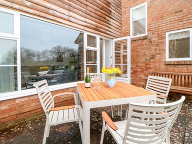An outdoor patio with four chairs around a wooden table with a vase of flowers and a bottle with glasses at Casalmare in Exmouth