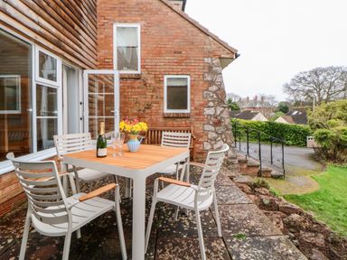An outdoor patio area with a table and four chairs a bottle of champagne and flowers on the table outside a brick house with stairs and greenery at Casalmare in Exmouth