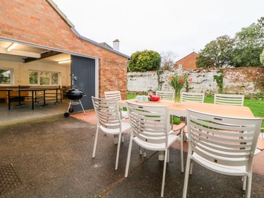 An outdoor patio with a dining table and chairs a teapot and cups on the table a small charcoal grill and an open garage with a ping pong table at Casalmare in Exmouth