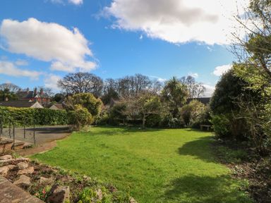 A garden with grass shrubs and trees under a blue sky at Casalmare in Exmouth