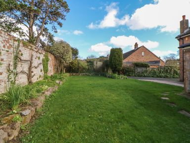 A garden with grass and plants along a brick wall with houses in the background at Casalmare in Exmouth