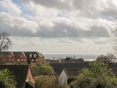 A view of rooftops with trees and the sea in the background under a cloudy sky at Casalmare in Exmouth