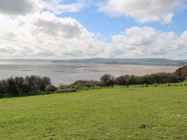 A grassy field with bushes overlooking a beach and water under a cloudy sky at Casalmare in Exmouth