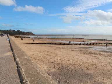 A sandy beach with wooden groynes and people walking near the shore at Casalmare Exmouth