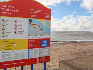A beach sign with safety information and a map next to a sandy shore at Maer Rocks in Exmouth