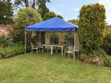 A garden area with a blue canopy tent and several white chairs around tables at Casalmare in Exmouth