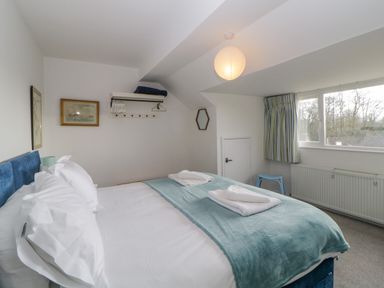 A bedroom with a double bed pillows and folded towels a blue blanket a window with striped curtains and a wall shelf with hangers at Casalmare in Exmouth
