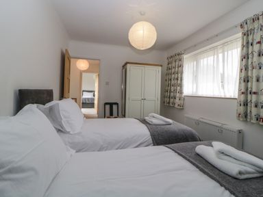 A bedroom with two single beds a white wardrobe and a window with patterned curtains at Casalmare in Exmouth