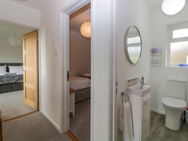 A small bathroom with a toilet and sink next to a hallway showing two bedrooms at Casalmare in Exmouth
