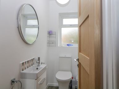 A small bathroom with a toilet sink round mirror wooden door and frosted window at Casalmare in Exmouth