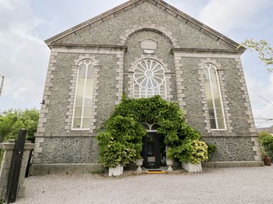 Stone building with arched windows and greenery around the entrance at Capel Mawr Basement 19 in Llanrug