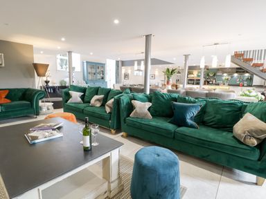 A living area with green sofas a black coffee table with wine and glasses and a blue ottoman at Capel Mawr Basement 19 in Llanrug