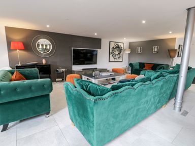A living room with green sofas orange cushions and poufs a large television and a round mirror at Capel Mawr Basement 19 in Llanrug