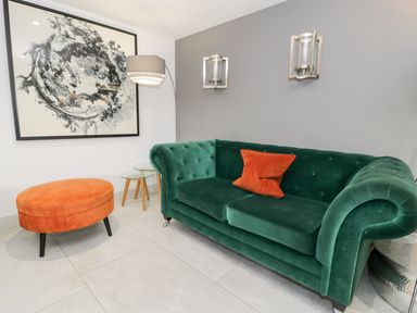 A living room with a green sofa and orange ottoman with a framed artwork on the wall at Capel Mawr Basement 19 in Llanrug