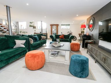 A living room with green sofas orange and blue poufs white coffee table and a motorcycle at Capel Mawr Basement 19 in Llanrug