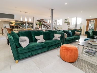 A living room with green sofas, an orange pouf and a coffee table with magazines at Capel Mawr, Basement 19 in Llanrug