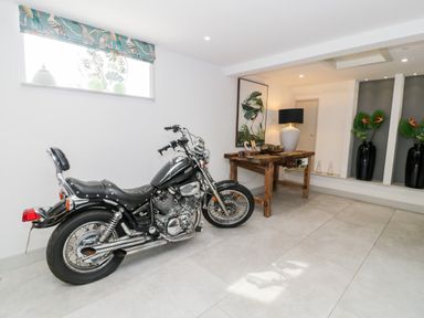 A basement room with a motorcycle, a wooden table with a lamp and framed bird artwork, and decorative vases with plants at Capel Mawr Basement 19 Llanrug