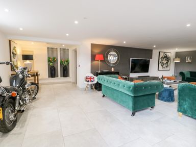 A living room with green sofas a motorcycle a white chair with a union jack cushion and vases with plants at Capel Mawr Basement 19 in Llanrug