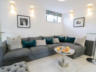 A living room with a grey sectional sofa and a round metal coffee table with croissants and orange juice glasses at Capel Mawr Basement 19 in Llanrug
