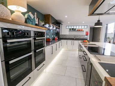 A modern kitchen with double ovens a countertop lamp and kitchen utensils at Capel Mawr Basement 19 in Llanrug