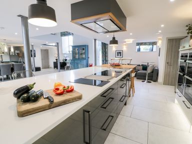 A kitchen with a large island countertop with vegetables on a cutting board and seating at Capel Mawr Basement 19 in Llanrug