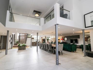 An open plan living space with a dining table, green sofas, staircase, and pillars at Capel Mawr, Basement 19 in Llanrug