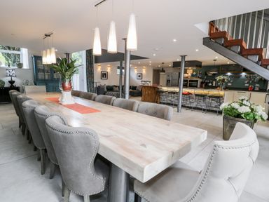 A large dining table with gray chairs and a plant centerpiece in an open kitchen and living area at Capel Mawr Basement 19 in Llanrug