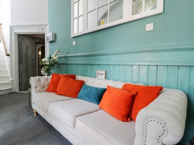 A sitting area with a beige sofa with orange and blue cushions and a vase of flowers at Capel Mawr Basement 19 in Llanrug