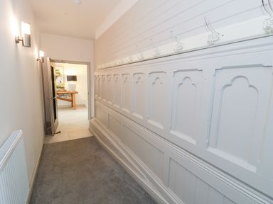 A hallway with numbered coat hooks along one wall and a table with a lamp in the room beyond at Capel Mawr Basement 19 in Llanrug